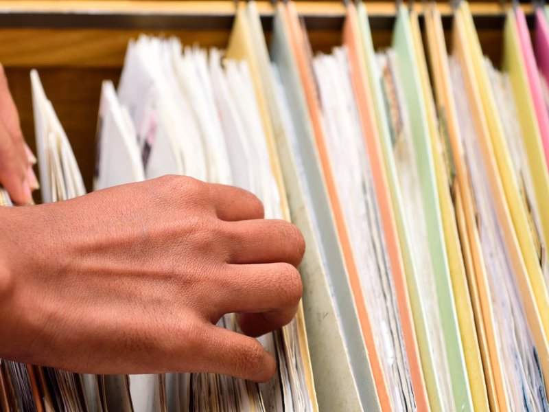 Hands are reviewing colorful files inside a filing cabinet.