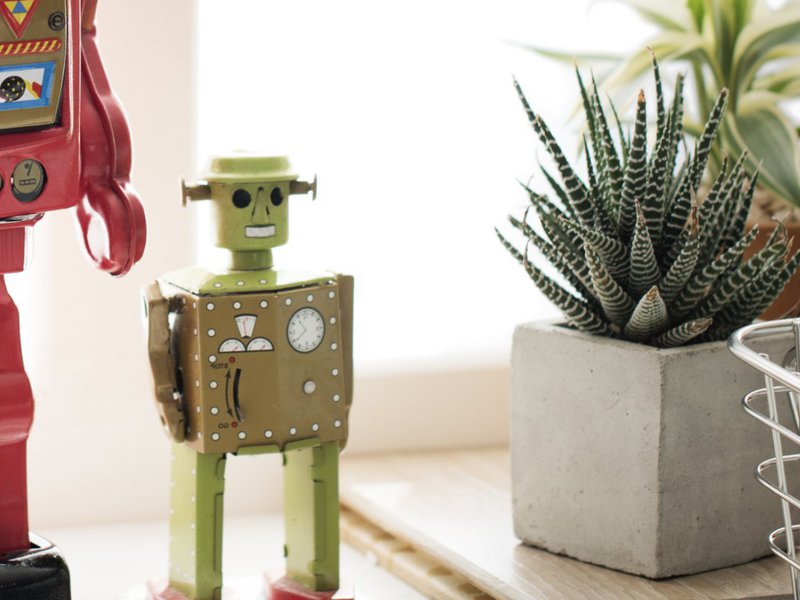 A small green robot, overlooking some paperwork, perhaps about to file a FOIA request. Cut off is a larger red robot standing next to it, perhaps getting ready to file a FOIA appeal.