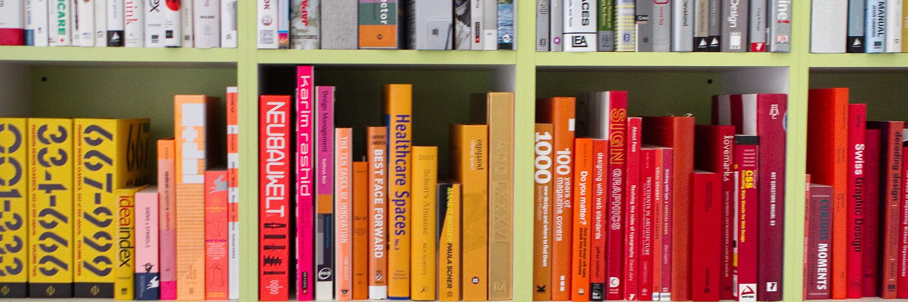A picture of a collection of books, organized by color on green square shelves.