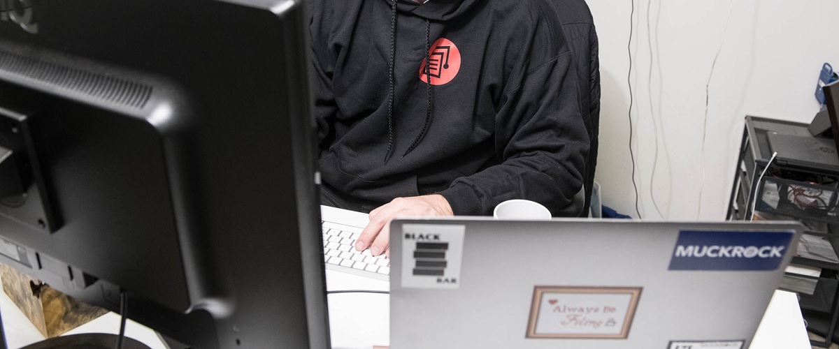 photo showing several computers on a desk with a person in a MuckRock branded sweatshirt at the keyboard.