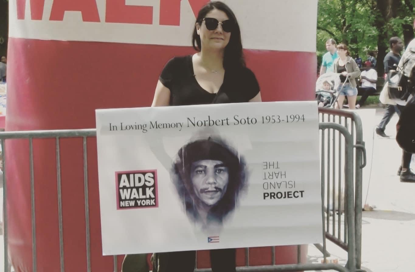 A photo of Elsie Soto holding a sign featuring a photo of her father, Norberto