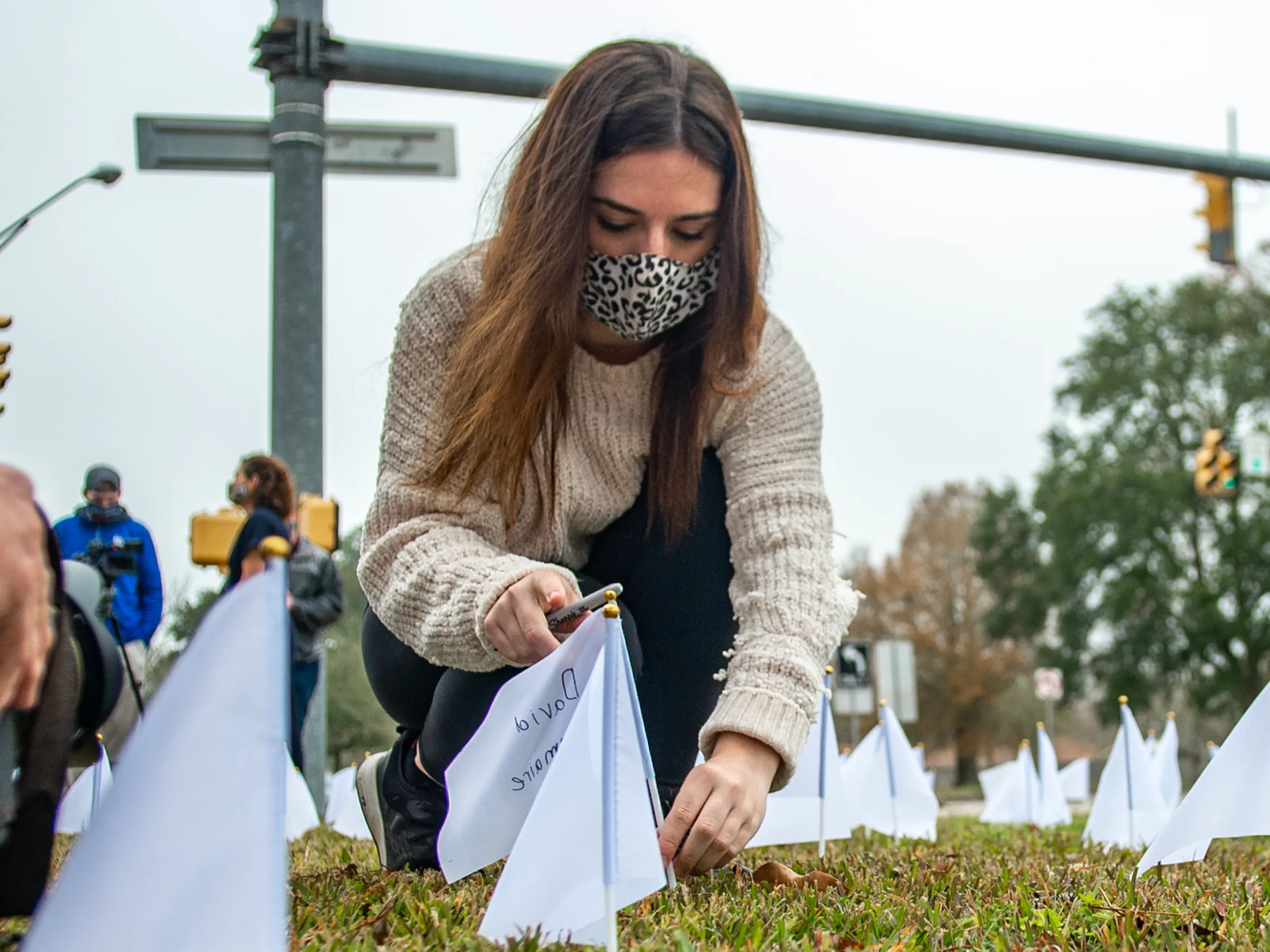 Madi Conrad plants a white flag on Jan. 24, 2021, outside St. Barnabas Episcopal Church in Lafayette, Louisiana, where 210 flags stood as a memorial to those who lost their lives to COVID-19 in Lafayette Parish. 